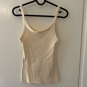 Beige ribbad linnetopp från H&M - Säljer ett beiget ribbat linne från H&M. Linnet har smala axelband och en rundad halslinje.