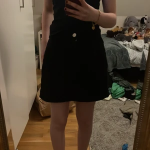 Svart kjol från Shein - Snygg svart kjol från Shein i storlek S. Kjolen har en enkel design med en knappdetalj framtill. Perfekt för att matcha med olika toppar och accessoarer.