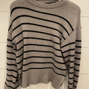 Grå och svart randig tröja från 157 - Säljer en snygg grå tröja med svarta ränder från 157. Tröjan har en rund hals och långa ärmar, perfekt för en stilren look. Den är ribbad vid halsen och ärmsluten för extra komfort.