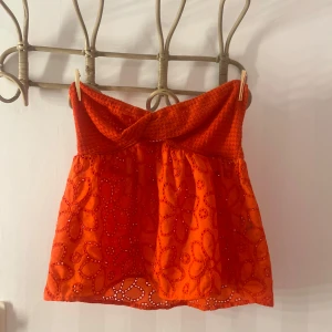 Orange axelbandslös topp - Snygg orange/röd axelbandslös topp med broderade blommor och en luftig design. Perfekt för varma dagar med sin lätta och bekväma passform.