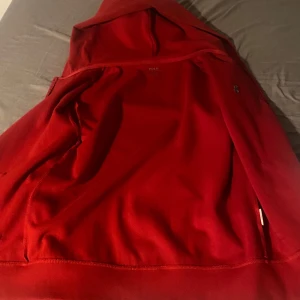Röd hoodie från Polo Ralph Lauren - Säljer en snygg röd hoodie från Polo Ralph Lauren med dragkedja och broderad logga på bröstet. Perfekt för en casual look med sin bekväma passform och huva.