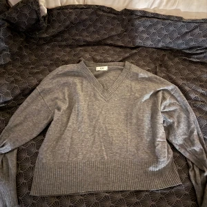 Grå V-ringad tröja från NELLY  - Säljer en stilren grå V-ringad tröja från A.P.C. Tröjan har långa ärmar och ribbade detaljer vid ärmslut och nederkant. Storlek S, knappt använd. 