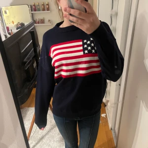 Mörkblå tröja med amerikansk flagga - Säljer en mörkblå tröja med en stor amerikansk flagga på framsidan. Tröjan har långa ärmar och en rund halsringning. Perfekt för en avslappnad stil.