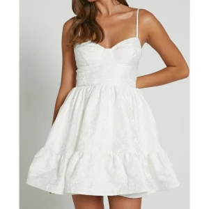 Vit klänning från Showpo - Säljer en söt vit klänning från Showpo med smala axelband och volangdetaljer. Klänningen har en vacker blommig struktur och en kort, luftig design som passar perfekt för sommarens festligheter och STUDENTEN!! Helt oanvänd med prislapp kvar