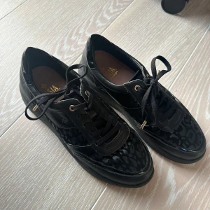 Svarta sneakers med leopardmönster från Dasia - Snygga svarta sneakers från Dasia med leopardmönster och snörning. Skorna har en glansig finish och en robust sula som ger bra komfort. Perfekta för att ge din outfit en trendig touch. Storlek 39. Knappt använda