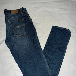 Blå jeans från Nudie Jeans - Snygga blå jeans från Nudie Jeans med klassisk femficksdesign och orange sömmar. Perfekta för en avslappnad stil. De har en normal passform och är tillverkade i slitstarkt denim. Storlek 30/32! Och är i bra skick! Var inte rädd att kontakta mig vid frågor!! Syns i dm!🔥🔥😉