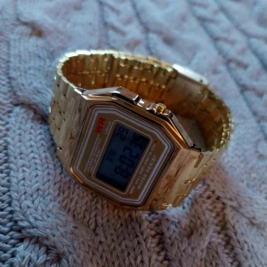 Guldfärgad digital klocka - Snygg guldfärgad digital klocka med metallarmband och rektangulär urtavla. Klockan har en tydlig digital display och är perfekt för en stilren look.