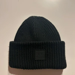 Svart ribbad mössa från Acne Studios - Snygg svart ribbad mössa från Acne Studios med ett stilrent uttryck. Perfekt för att hålla värmen under kyliga dagar. Mössan har en enkel design med en liten etikett på insidan.