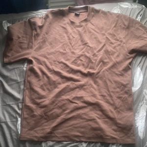 Brun oversized t-shirt från FSBN - Säljer en brun oversized t-shirt från FSBN. Den är tillverkad i en mjuk blandning av bomull och polyester. Perfekt för en avslappnad stil. T-shirten har korta ärmar och en rund halsringning.