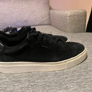 Svarta sneakers från Gant - Snygga svarta sneakers från Gant i mocka med vit sula och snörning. Perfekta för en stilren look. Skorna har en klassisk design med diskret logga på sidan.