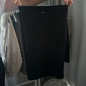 Svart kjol från Guess - Snygg svart kjol från Guess med ett subtilt leopardmönster. Kjolen har en tight passform och är perfekt för att ge en stilren look. Den är tillverkad i ett mjukt material som ger en bekväm känsla. Nypris är 995kr. Hittade ej storleken men tror storlek S. Man kan också ha den som en topp