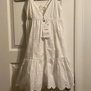 Vit klänning från Zara! Student!? Prislappar kvar  - Säljer en söt vit klänning från Zara med broderade detaljer och volang. Klänningen har en v-ringad design och knytning i ryggen. Perfekt för sommarens varma dagar eller vårens Student! 