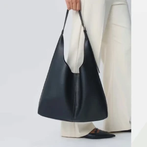 Svart axelväska i skinn - Stilren svart axelväska i skinn med enkel design. Perfekt för att bära med sig det nödvändigaste med stil. Väskan har en lång rem för bekväm axelpassning. Perfekt som skolväska då den är rymlig. Från Gina Tricot där nypris låg på 400kr, mitt pris 300kr då den knappt är använd. 