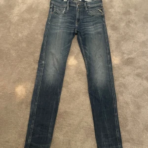 Blå jeans från Replay - Snygga blå jeans från Replay i modellen Anbass. De har en klassisk femficksdesign med dragkedja och knapp framtill. Jeansen har en lätt tvättad look som ger en avslappnad stil. Perfekta för en casual outfit.