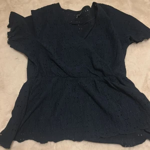 Mörkblå blus från Vero Moda - Säljer en mörkblå blus från Vero Moda med v-ringning och korta ärmar. Blusen har ett fint broderat mönster och är i toppen sick då den använts 1 gång. 