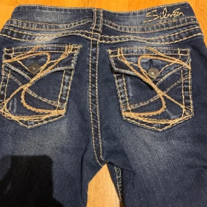 Mörkblå jeans från Silver Jeans - Snygga mörkblå jeans från Silver Jeans med unika broderade bakfickor och kontrastsömmar. Perfekta för en avslappnad stil med en touch av detaljer. Passar bra till både sneakers och boots.