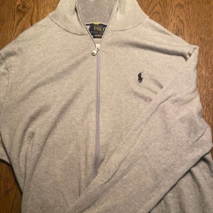 Grå tröja med dragkedja från Polo Ralph Lauren - Säljer en stilren grå tröja från Polo Ralph Lauren i mjuk pima bomull. Tröjan har en dragkedja framtill och det klassiska logotypbroderiet på bröstet. Perfekt för en avslappnad och snygg look. Jätte bra skick. Säljs pågrund av att jag vill ha pengar till annat