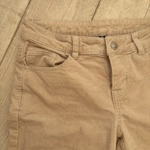 Beige manchesterbyxor - Snygga beige manchesterbyxor med klassisk design. Byxorna har en rak passform och är perfekta för en stilren look. De har en knapp och dragkedja framtill samt fickor på sidorna