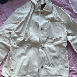 Beige jacka från Bershka - Snygg beige jacka från Bershka med knappar framtill och en klassisk krage. Jackan har två fickor på sidorna och en bröstficka. Perfekt för en stilren look. 