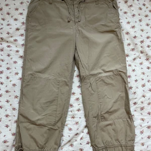 Beige cargopants från Esprit - Säljer ett par beige cargopants från Esprit. Byxorna har flera praktiska fickor och justerbar midja med snörning. Perfekta för en avslappnad stil. En knapp saknas i midjan men är annars hela.