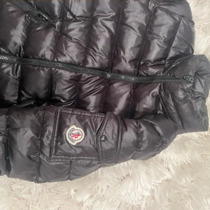 Svart pufferjacka från Moncler - Säljer en snygg svart pufferjacka från Moncler. Jackan har en glansig finish och är utrustad med dragkedja framtill samt två praktiska fickor med dragkedjor. Perfekt för kyligare dagar. Den är i bra skick!!! 
