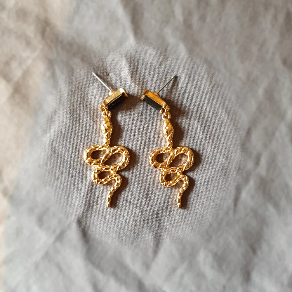 Snygga guldiga örhängen i form av slingrande ormar. Perfekta för att ge en unik touch till din stil. De har en elegant och iögonfallande design som passar bra till olika tillfällen💕. Asusteet.