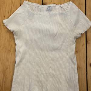 Säljer en söt vit ribbad topp från Lindex i storlek 158/164. Toppen har korta ärmar och en enkel design som passar perfekt till vardags. Den är tillverkad i ett mjukt och bekvämt material.