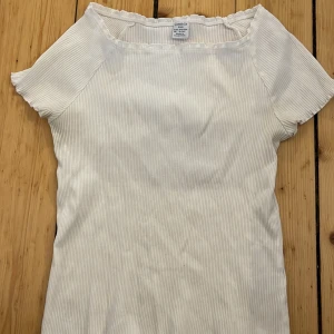 Vit ribbad topp från Lindex - Säljer en söt vit ribbad topp från Lindex i storlek 158/164. Toppen har korta ärmar och en enkel design som passar perfekt till vardags. Den är tillverkad i ett mjukt och bekvämt material.