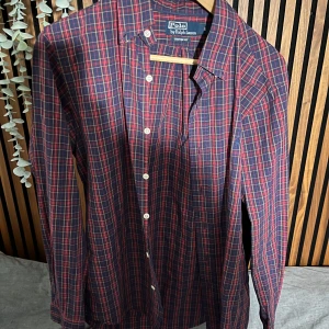 Rutig skjorta från Polo Ralph Lauren - Snygg rutig skjorta från Polo Ralph Lauren i rött och blått. Skjortan har långa ärmar och knappar framtill. Perfekt för en stilren look.