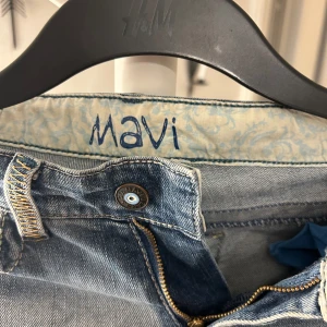 Blå jeans från Mavi - Snygga blå jeans från Mavi med en klassisk femficksdesign. De har en dragkedja och knapp framtill samt dekorativa sömmar på bakfickorna. Perfekta för en avslappnad stil.