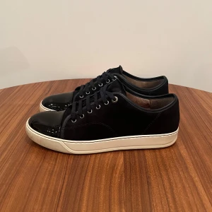 Lanvin Cap Toe Navy UK 8 - Säljer dessa riktigt snygga och stilrena Lanvin Cap Toe Navy. Köpta nya av mig på Lanvins hemsida. Skick: 8/10 då de är slitna under sulan men är annars i riktigt fint skick. Storlek UK 8 vilket motsvarar 42 men passar 43. Nypriset på dessa ligger runt 5000. Extra oanvända skosnören medföljer. Inga byten! Hör av dig vid några funderingar!