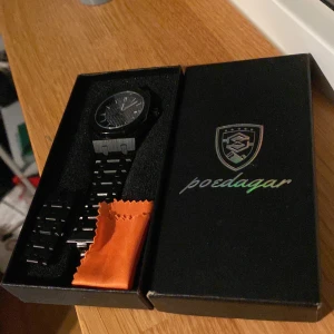 Svart klocka från Poedagar - Snygg svart klocka från Poedagar med stilren design. Klockan har en svart urtavla med vita markeringar och datumvisning. Armbandet är i svart metall och kommer i en elegant förpackning. Perfekt för en stilren look.