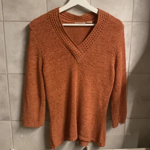 Orange stickad tröja från Tweeds - Säljer en snygg orange stickad tröja från Tweeds med v-ringad design. Tröjan har trekvartsärmar och en fin stickad struktur som ger en unik look. Perfekt för kyligare dagar!