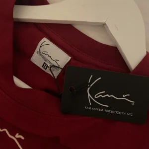 Vinröd oversize t-shirt från Karl Kani - Snygg oversize vinröd t-shirt från Karl Kani med deras ikoniska logga tryckt på bröstet. Perfekt för en avslappnad stil. T-shirten är kortärmad och gjord i mjukt material. Den är helt oanvänd och har kvar etiketten
