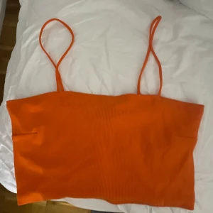 Orange ribbad tubtopp - Snygg orange ribbad tubtopp med smala axelband. Perfekt för sommardagar och kan enkelt matchas med olika outfits. Har använts ett par gånger men i bra skick. 