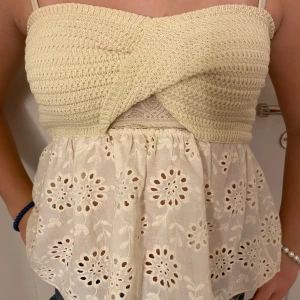 Beige stickad topp med spetsdetaljer - Säljer en söt beige stickad topp med smala axelband och spetsdetaljer. Toppen har en twist framtill och ett vackert broderat mönster på den nedre delen. Perfekt för varma sommardagar!