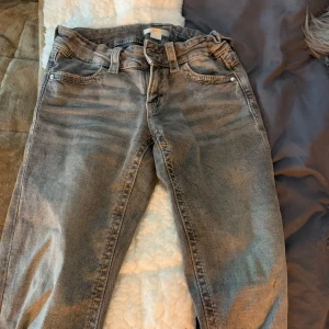 Grå jeans med flätade bakfickor - Snygga grå jeans med unika flätade detaljer på bakfickorna. De har en klassisk femficksdesign och bälteshällor. Perfekta för en avslappnad stil.