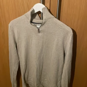 Beige tröja med dragkedja från Jack&Jones  - Säljer en stilren beige tröja från Jack&Jones med dragkedja vid halsen. Tröjan har långa ärmar och är perfekt för en avslappnad look. Passar bra till både jeans och chinos.