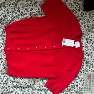 Röd kofta från H&M - Säljer en snygg röd kofta från H&M med korta ärmar och knappar framtill. Perfekt för att lägga till en färgklick i din garderob. Koftan är i ett mjukt material och har en klassisk design.