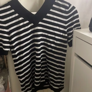 Svart och vit randig kortärmad tröja - Säljer en stilren svart och vit randig tröja med v-ringning. Tröjan har korta ärmar och är perfekt för en avslappnad look. Passar bra till jeans eller shorts.