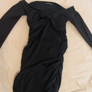 Svart klänning från Shein - Snygg svart klänning från Shein med offshoulder-design och långa ärmar. Klänningen har en åtsittande passform med rynkade detaljer som ger en elegant look. Perfekt för en kväll ute eller en speciell tillställning.