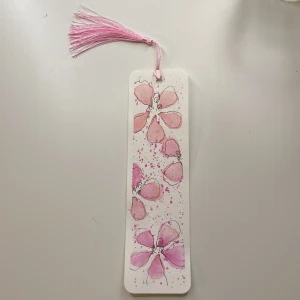 Blommigt bokmärke med rosa tofs - Charmigt bokmärke med handmålade blommor i rosa och lila nyanser. Bokmärket har en dekorativ rosa tofs i toppen, perfekt för att hålla koll på var du är i din bok. En fin detalj för bokälskare. Tofsen går även att bytas ut till en annan färg om så önskas!