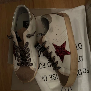 Golden Goose sneakers med leopardmönster - Snygga Golden Goose sneakers i vitt med röda glittriga stjärnor på sidorna. Skorna har leopardmönstrade snören och en brun mockadetalj på tån. Silverfärgade detaljer på hälen ger en extra touch. Nya utan prislapp, använda en gång, allt tillbehör finns. Pris kan diskuteras. 