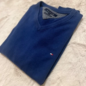 Blå tröja från Tommy Hilfiger - Snygg blå tröja från Tommy Hilfiger i bomull och kashmir. Den har en v-ringad hals och ett diskret logotypbroderi på bröstet. Perfekt för en stilren look.