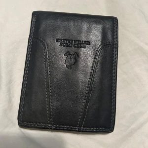 Svart plånbok från Beverly Hills Polo Club - Elegant svart plånbok i skinn från Beverly Hills Polo Club. Den har flera fack för kort och en sektion för sedlar. Perfekt för den stilmedvetna som vill ha en praktisk och snygg accessoar.