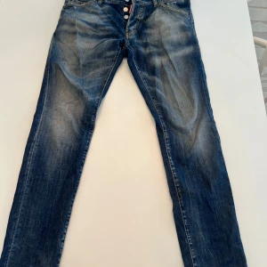 Blå jeans från Dsquared2 - Snygga blå jeans från Dsquared2 med en cool tvättad look och röda färgstänk. De har en klassisk femficksdesign och knappar i gylfen. Perfekta för en avslappnad stil med en touch av edge.