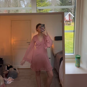 Rosa omlottklänning - Säljer en söt rosa omlottklänning med volangdetaljer och prickigt mönster. Klänningen har långa ärmar och en v-ringad design som ger en fin känsla. Perfekt för vårens och sommarens tillfällen! 💖Använd 1 gång!