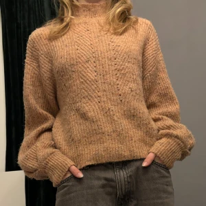 Beige stickad tröja - Säljer en mysig beige stickad tröja med lång ärm och ribbade detaljer vid ärmslut och nederkant. Perfekt för kyliga dagar och ger en avslappnad look. Passar bra till jeans eller kjol.