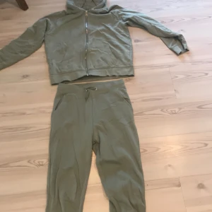 Grönt set  - Säljer ett par gröna mjukisbyxor med matchande hoodie. Byxorna har en bekväm passform med resår i midjan och snörning. Hoodien har en dragkedja framtill och en mysig huva. Båda i 160. 