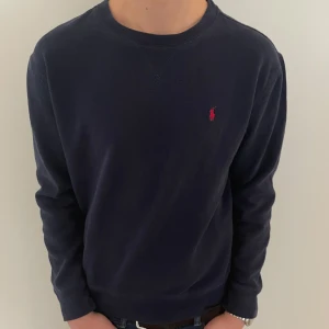 Mörkblå tröja från Ralph Lauren - Säljer en mörkblå tröja från Ralph Lauren med den klassiska röda logotypen på bröstet. Tröjan har långa ärmar och rund halsringning. Perfekt för en avslappnad och snygg outfit. Pris kan diskuteras vid snabb affär!